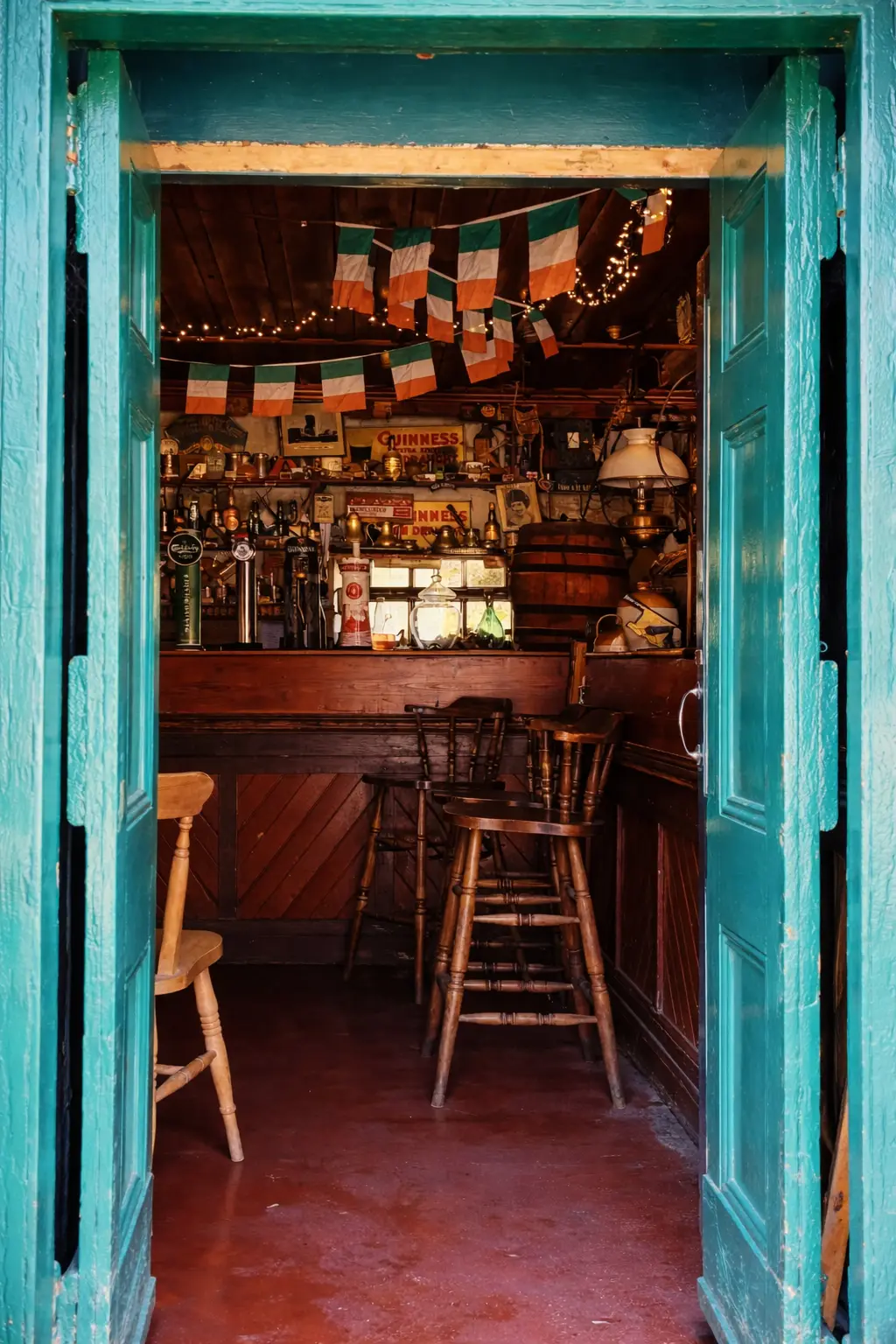 View through turquoise-painted double doors into Stanford Village Inn bar with Irish tricolours, Guinness taps, brass lamps, and traditional wooden stools on red stone floor