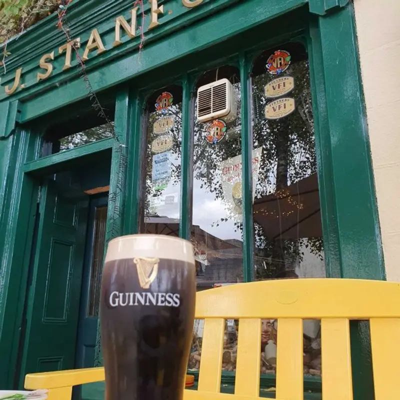 Close-up of Stanford Village Inn green-painted front door and J. Stanford signage with a pint of Guinness on a yellow bench